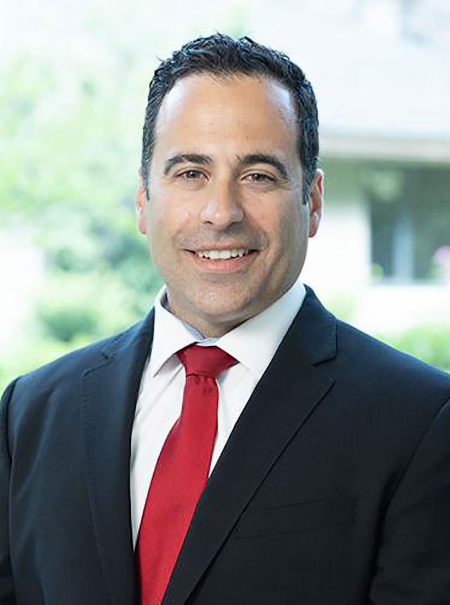 Steve Sterious, a male urologist with a red suit and black suit jacket, smiling