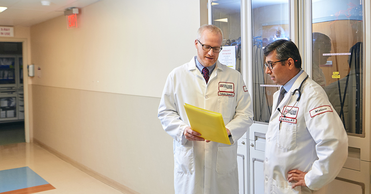 A photograph of two Fox Chase doctors standing in a hallway and looking at a file together.