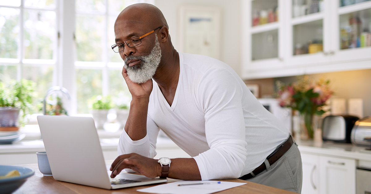 A person leans down to use their laptop on a kitchen counter.