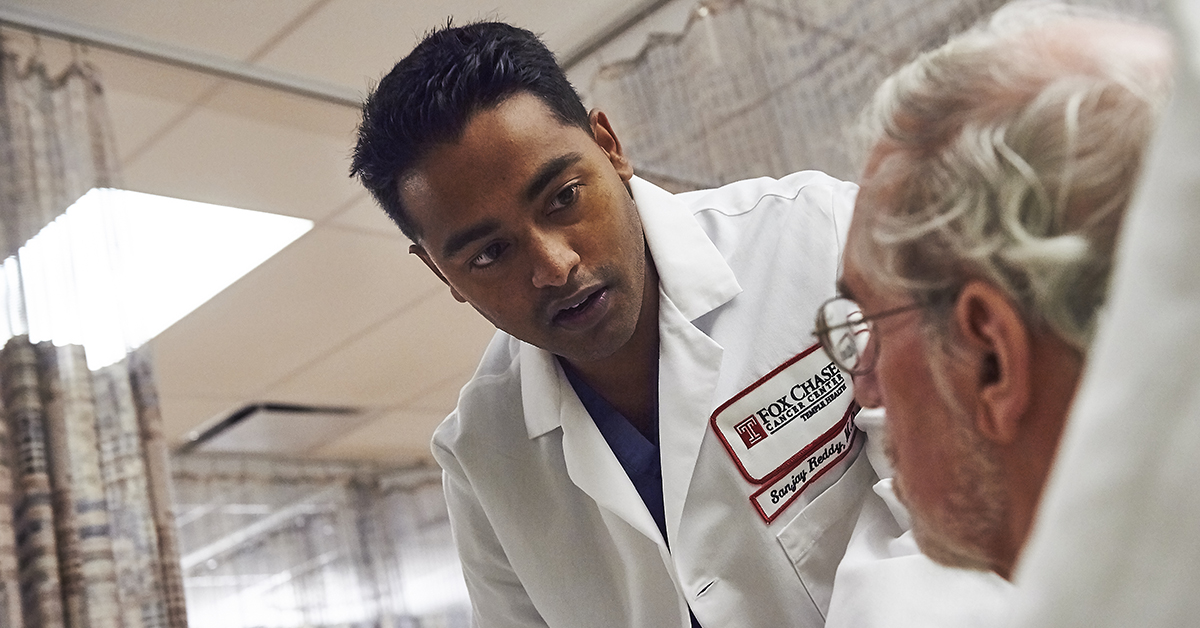 A photo of Dr. Sanjay Reddy leaning over a patient laying down on a hospital bed.