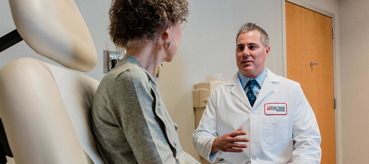 A side view photograph of a patient sitting in a tan medical chair, speaking with a Fox Chase doctor on the other side of them.