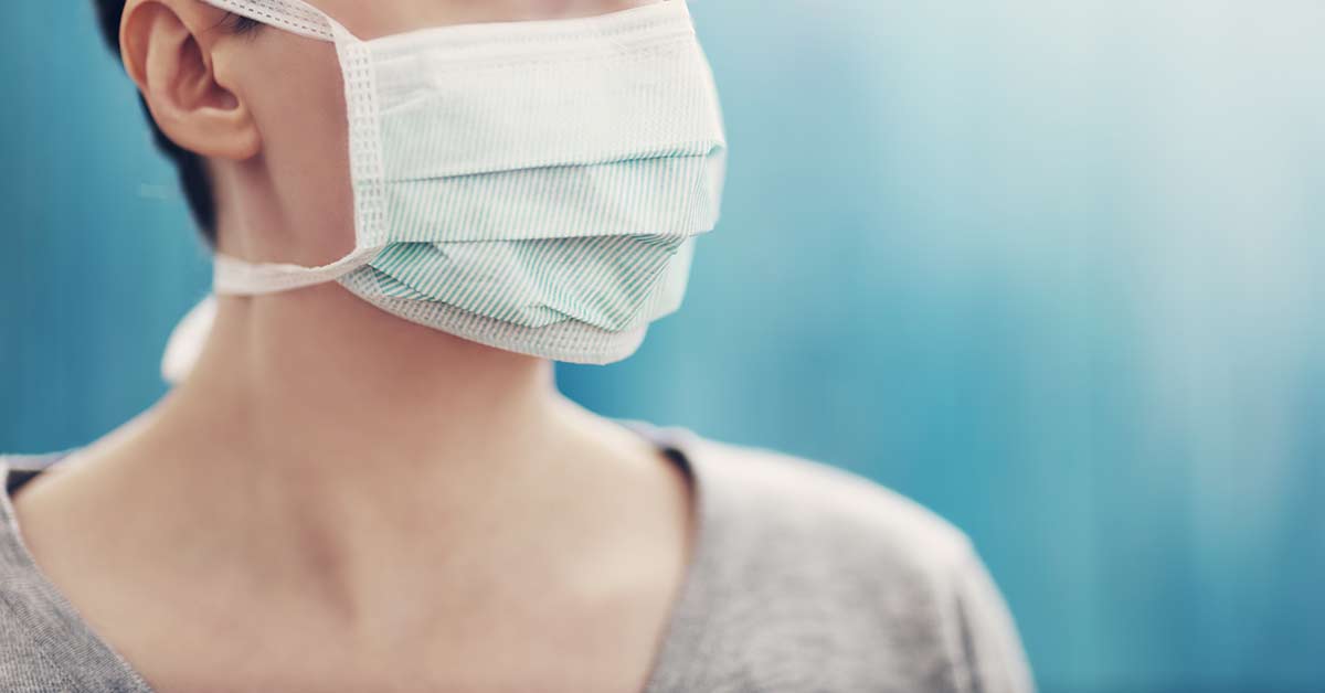 A portrait shot of a person's face cut off above the nose, covered by a mask and looking off to the side.