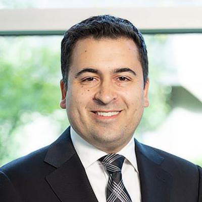 A close-up of Justin I. Friedlander, a male urologist, wearing a black suit with a white shirt, smiling. 