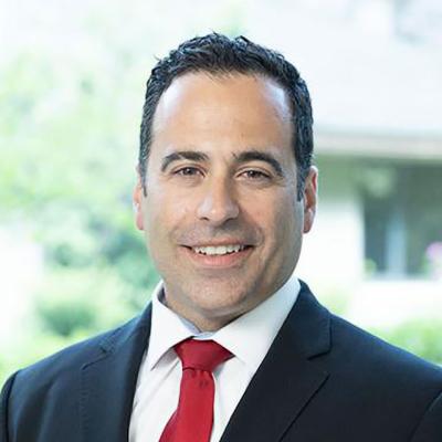 Steve Sterious, a male urologist with a red suit and black suit jacket, smiling