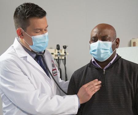A Fox Chase doctor holds a stethoscope to a patient's chest inside of a medical room.