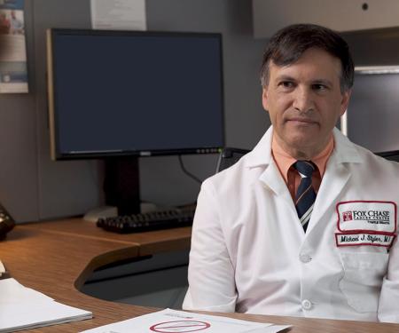A photograph of a Fox Chase doctor sitting behind a desk, speaking with someone on the other side of it.