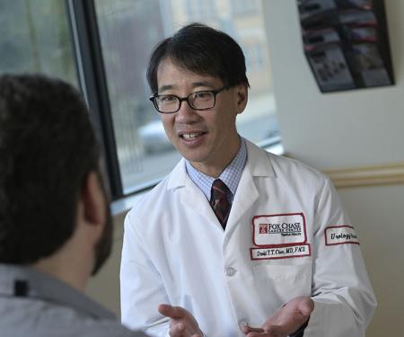 A Fox Chase doctor smiles as they speak with a patient, sitting across from each other in front of a window.