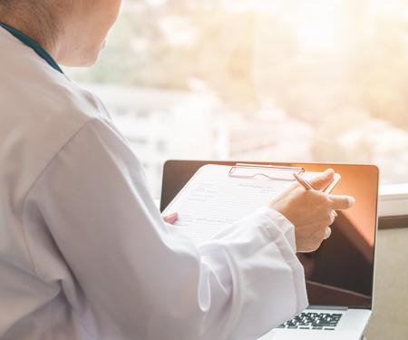 A photo from behind two people, with a clipboard and laptop in front of them and bright sunlight coming in from the window.
