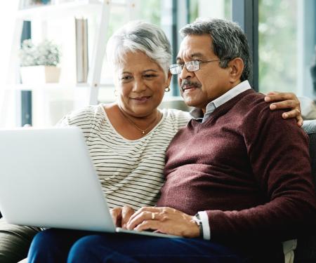 Two people huddle closely together on the couch, using a laptop.