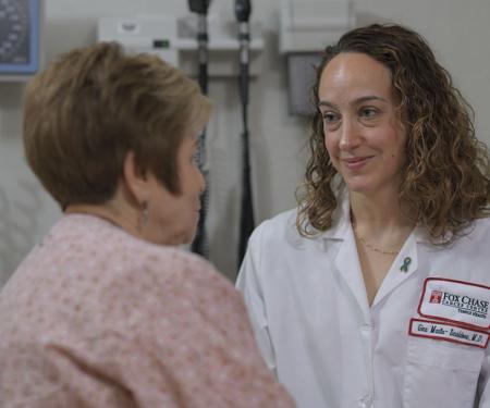 A photo of a Fox Chase doctor smiling at a patient sitting on a medical chair.
