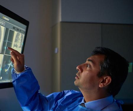 A Fox Chase doctor stands in a dark room, interacting with a screen displaying medical imaging results.