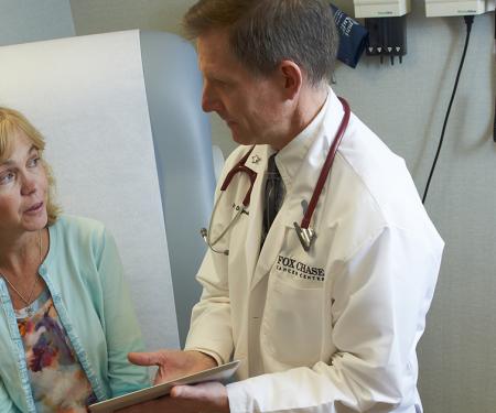 A Fox Chase doctor speaks closely with a patient, gesturing to a clipboard in his hands.