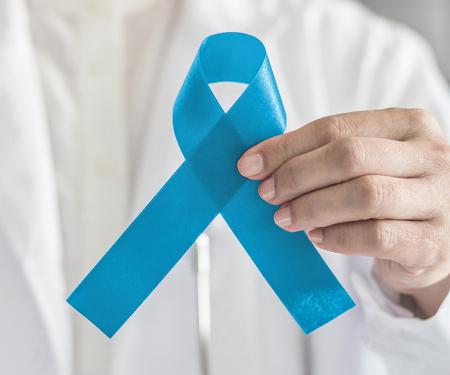 A closeup photo of a medical professional's chest, where they hold a sky blue ribbon in front of them.