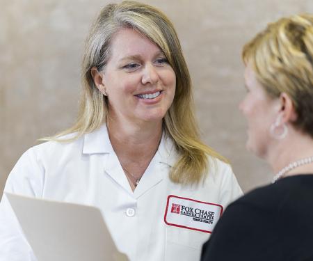A photograph of a Fox Chase doctor holding a file, smiling at a patient.