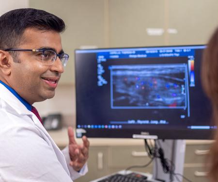 A Fox Chase doctor converses with another person in front of a screen with results from a medical imaging test on it.