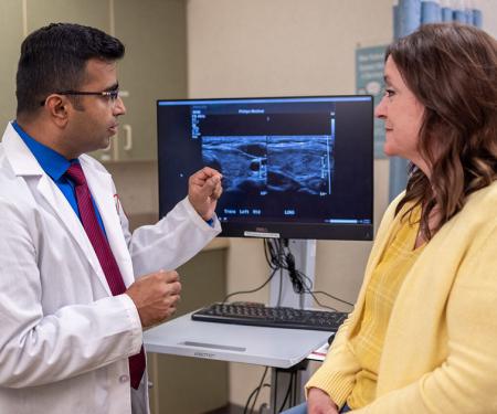 A Fox Chase doctor converses with a patient in a medical room with results from an imaging test on a screen between them.