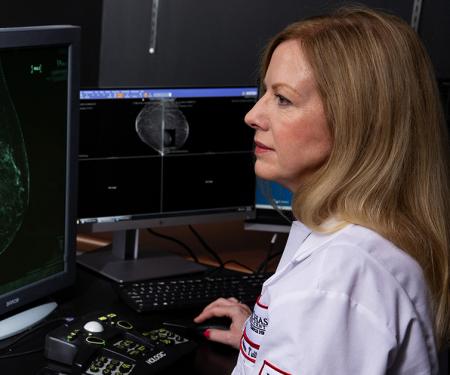 A photograph of a medical professional looking at two screens with images from a mammogram displayed on both.