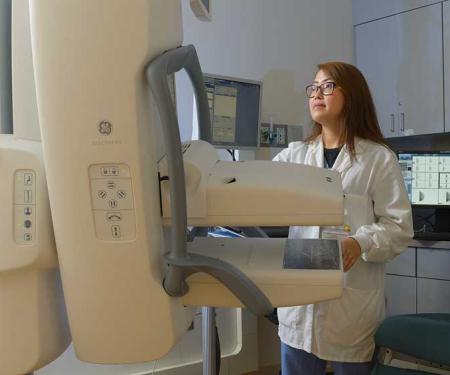 A photo of a medical professional looking at a mammogram machine.