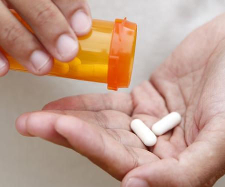 A closeup photo of two white capsules being shaken from a pill bottle in one hand into the other.