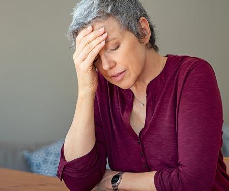 A photo of a person wearing a wine colored shirt, leaning over a table with their head in their hand.