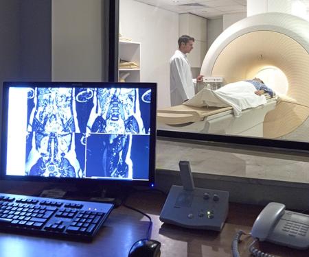 A photograph of a medical professional standing next to a patient inside of a large medical imaging machine.