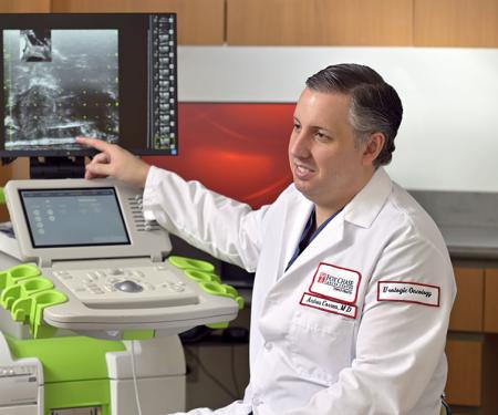 A photograph of a Fox Chase doctor speaking to a patient in a medical chair while gesturing at an image on a screen.