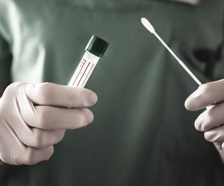 A close up photograph of medical professional's upper body, an empty collection vial and a long cotton swab in their hands.