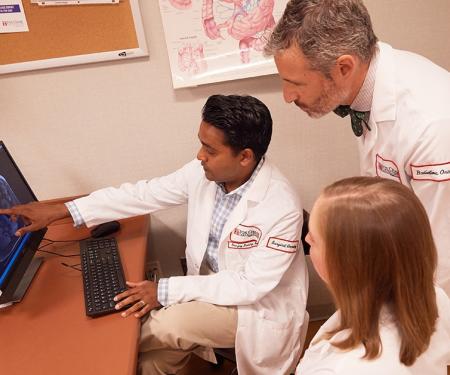 A photograph of three doctors around a computer discussing the displayed medical imaging results.