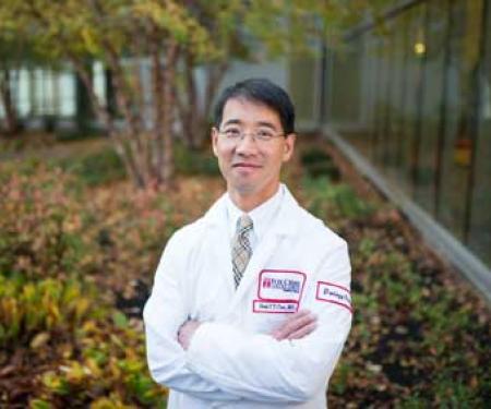 A photograph of a Fox Chase doctor standing outside, crossing their arms and smiling at the camera.
