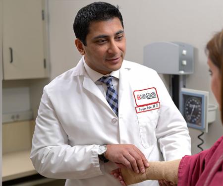 A Fox Chase doctor smiles as he examines a patients arm, which is covered in a tan medical wrap.
