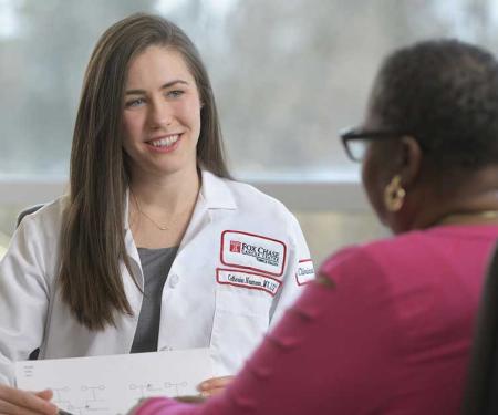 A photo of a Fox Chase doctor sitting across from a patient, smiling and holding a paper in their hands.