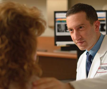 A closeup photo of a Fox Chase doctor gently putting his hand on a patient's shoulder.