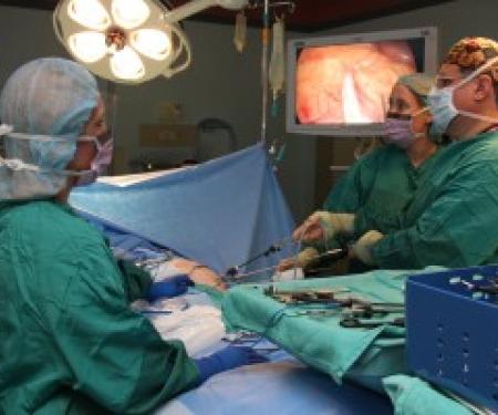 A photograph of three doctors performing surgery, looking up at two screens showing the feed from a laparoscope.