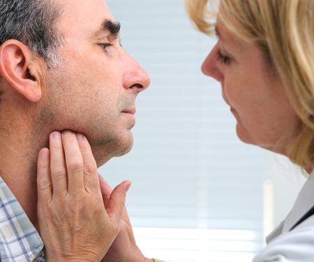A photograph of a medical professional using her hands to feel the underside of a patient's chin.