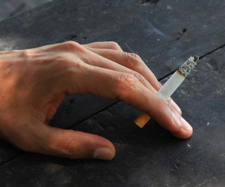 A closeup photo of a person's hand resting on a dark stone surface, holding a cigarette between their fingers.