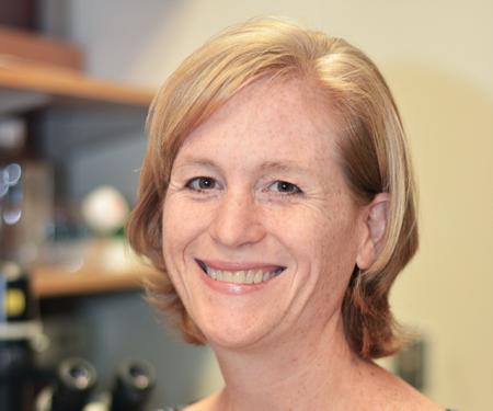 A portrait shot of Tiffiney Hartman standing in a laboratory, smiling at the camera.