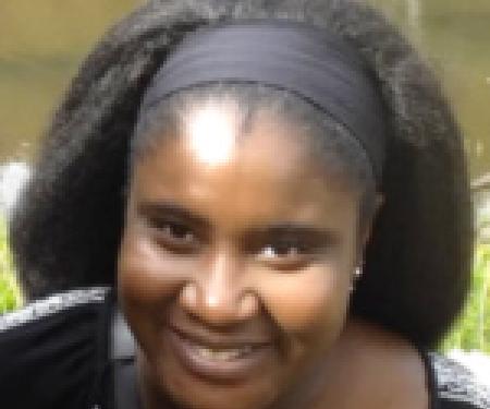A close up photograph of Sajitha Anthony's face, smiling at the camera as they stand outside.