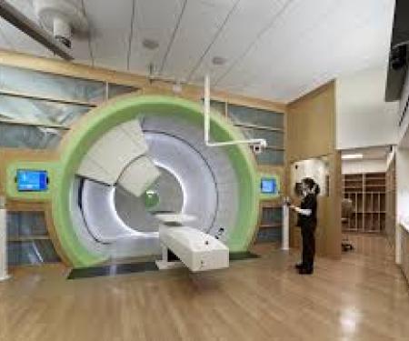 A zoomed out photo of a large green, white, and grey medical treatment device, with a medical professional standing next to it.