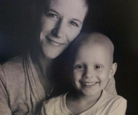 A sepia photograph of Sheila Koreck sitting with her four year old daughter in her lap, both smiling at the camera.