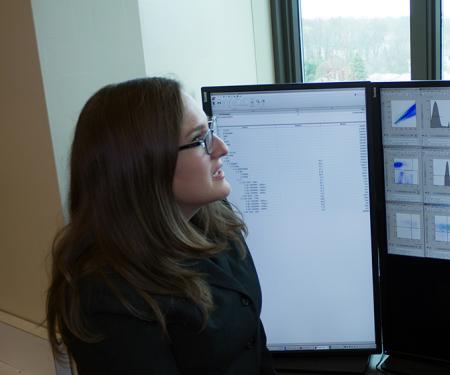 Two medical professionals stand close together in front of several screens, discussing the information displayed.