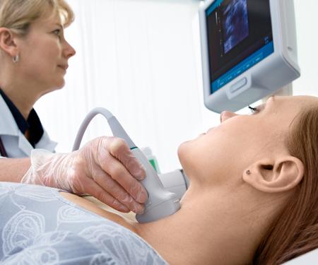 A photograph of a medical professional looking at a screen while giving a patient an ultrasound of their neck.