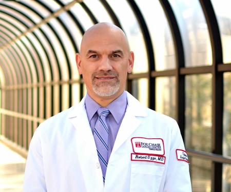A portrait shot of Dr. Robert Uzzo, standing on the right side of the frame in a blurry hallway with lots of windows.