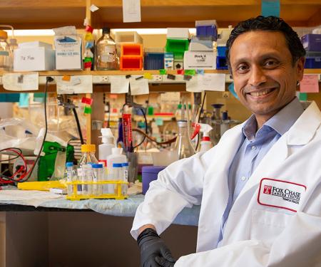 Close-up of Siddharth Balachandran sitting at a desk, wearing a white coat and smiling