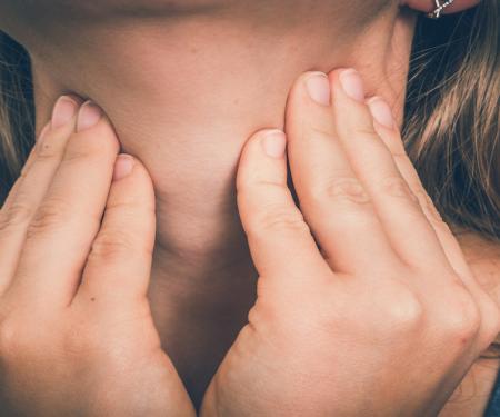 A closeup photo of a person pressing on either side of their neck with their fingertips.