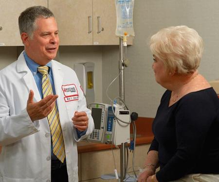 A photograph of a Fox Chase doctor smiling as he speaks with a patient receiving an IV in a medical room.