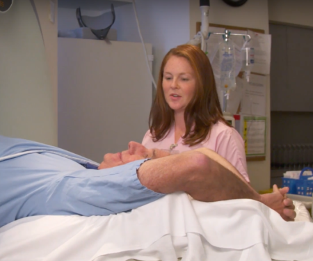 A side view photo of a patient going into a medical imagine machine, with a medical professional standing behind them.