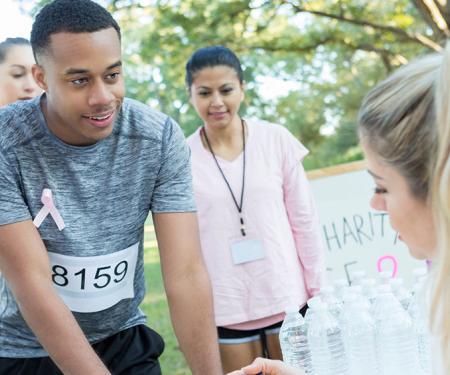 A photograph of three runners at a table with water bottles on it, with a person behind the table speaking to one of them.