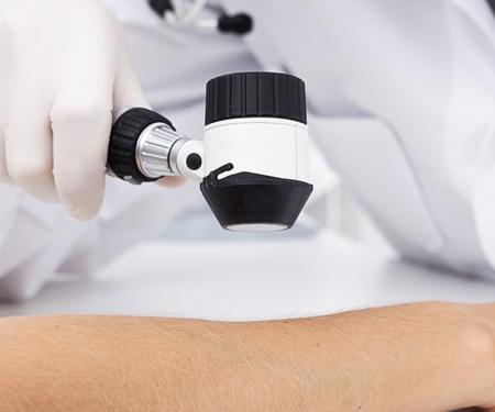 A closeup photo of a medical professional holding a handheld tool up to a patient's arm to help them examine it.