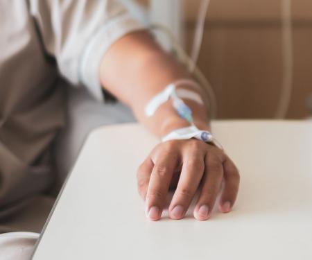 A closeup photo of a patient's arm as they sit in a chair and receive an IV through their wrist.