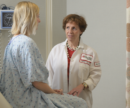 A photo of a Fox Chase doctor standing near a patient sitting in an exam chair, speaking with serious looks on their faces.